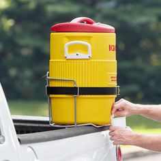 a man is holding a yellow and red cooler in the back of a white truck