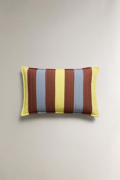 a brown and blue striped pillow sitting on top of a white bed next to a wall