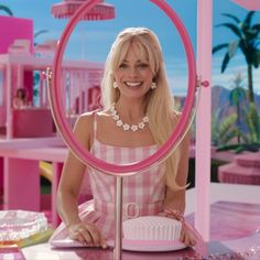 a woman sitting at a table with a cupcake in front of her and a pink background