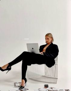 a woman sitting in a chair with her legs crossed and holding a laptop on her lap