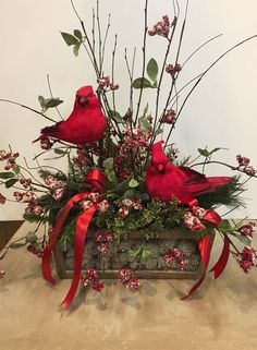 two red birds sitting on top of a wooden box filled with flowers