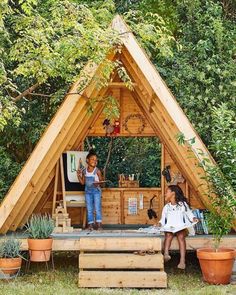 two children are standing on the roof of a small house made out of wooden planks