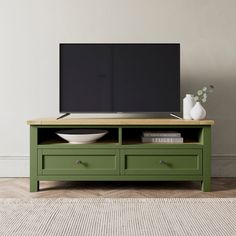 a flat screen tv sitting on top of a green entertainment center next to a white vase