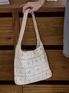 a hand holding a crocheted white purse on top of a wooden dresser next to books