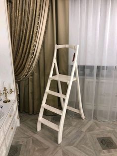 a ladder leaning against the wall in front of a window with drapes and curtains