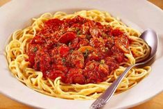 a white bowl filled with spaghetti and sauce on top of a wooden table next to a fork