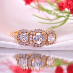 three stone diamond ring sitting on top of a white cloth with red flowers in the background