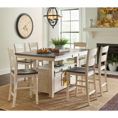 a dining room table and chairs with a clock on the wall above it in front of a fireplace