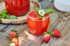 two glasses filled with liquid and strawberries on top of a wooden table next to other items