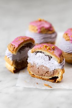 three donuts with pink icing and sprinkles on top of white paper