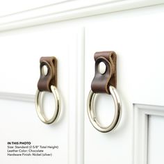 two metal handles on the front of a white cabinet with brown leather handle and ring