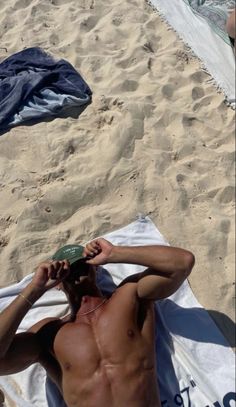 a shirtless man laying on top of a beach next to a towel and hat