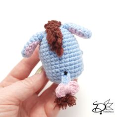 a hand holding a small crocheted blue and brown stuffed animal in it's right hand