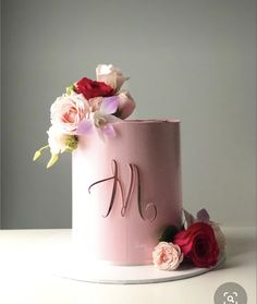 a pink cake decorated with flowers and the letter m on top is sitting on a white plate