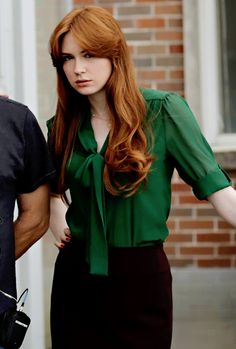 a woman with long red hair wearing a green shirt and black skirt is standing next to a man