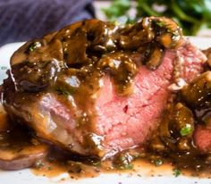 a piece of steak covered in mushrooms and gravy on top of a white plate