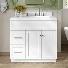 a white bathroom vanity with green walls and flowers on the counter top, in front of a mirror