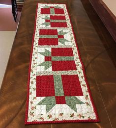 a long table runner made with red and green quilts on top of a wooden table