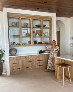 a woman standing in a kitchen with wooden cabinets