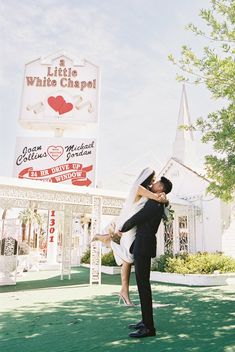 a bride and groom kissing in front of a white chapel sign at their wedding reception