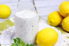 a glass bottle filled with white liquid next to lemons and parsley on a doily