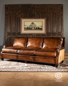 a brown leather couch sitting on top of a rug in front of a wooden paneled wall