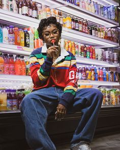 a man sitting on the floor in front of a store filled with drinks and sodas