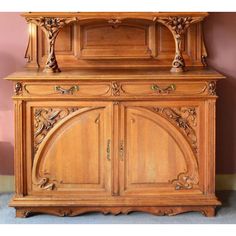 an old wooden cabinet with carvings on the top and bottom, against a pink wall