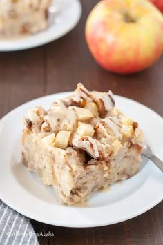 a piece of dessert sitting on top of a white plate next to an apple and cinnamon roll