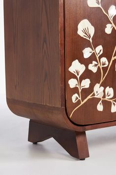 a wooden cabinet with white flowers painted on the front and side panels, along with two legs