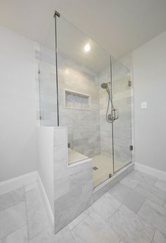 a walk in shower sitting next to a white tiled wall and floor with a glass door