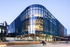 two people are walking in front of a building with glass walls and stairs leading up to it