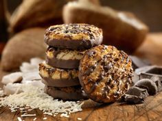 three chocolate covered cookies sitting on top of a wooden table next to some shredded coconut