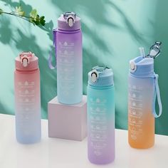 three different colored water bottles sitting next to each other on a white table with a plant in the background