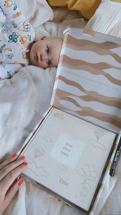 a baby laying in bed next to an open book with writing on it's cover