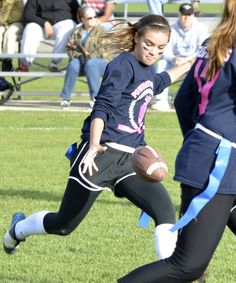 two girls are playing football on the field while people watch from the bleachers