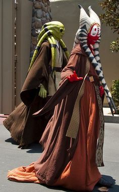 two people dressed in costumes walking down the street, one wearing a costume with an alien head