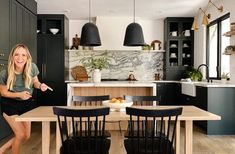 a woman standing in a kitchen next to a table with black chairs and an island