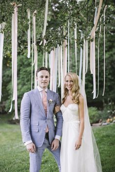 a bride and groom posing for a photo under a tree decorated with hanging streamers