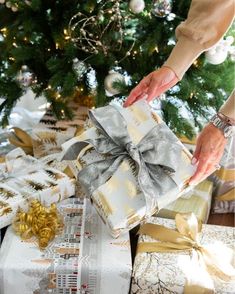 a person wrapping presents under a christmas tree with gold and silver ribbons on it's wrappers