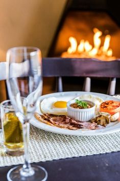 a white plate topped with eggs and meat next to a glass of wine on top of a table