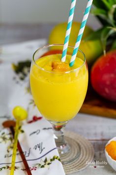 a glass filled with orange juice and two blue striped straws next to some fruit