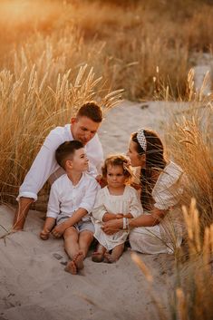 a family sitting in the sand with tall grass