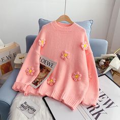 a pink sweater with flowers on it sitting on top of a blue chair next to books