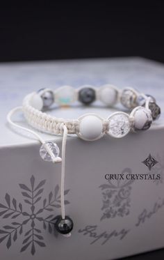 a white bracelet with black beads and silver accents on top of a card board box