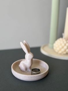 a white rabbit figurine sitting on top of a table next to a candle holder