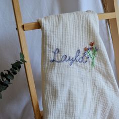 a white towel with embroidered name and flowers on it sitting on a wooden chair next to a potted plant