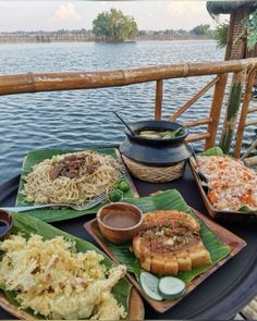 an assortment of food sitting on top of a table next to the water in front of a wooden fence