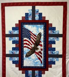 an american flag and eagle quilted on a wall hanging in front of a blue sky with clouds