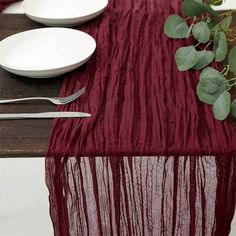 the table is set with plates, silverware and a red cloth draped over it